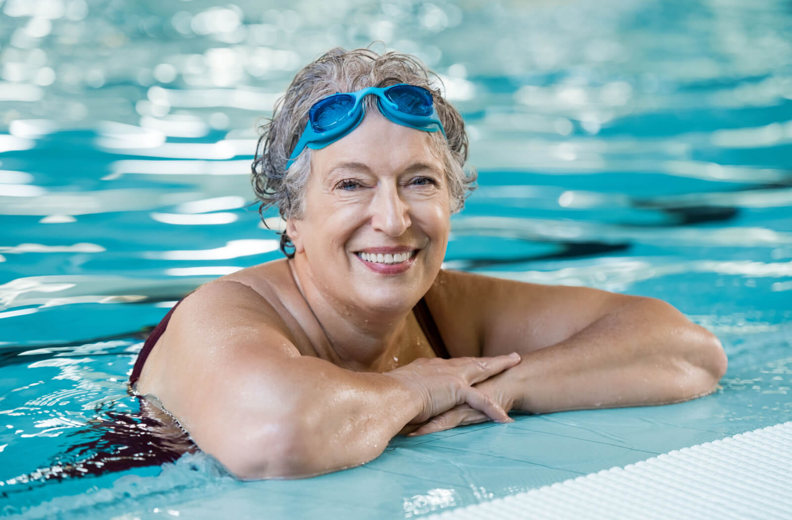 A senior wearing goggles at the swimming pool, smiling and looking directly at the camera