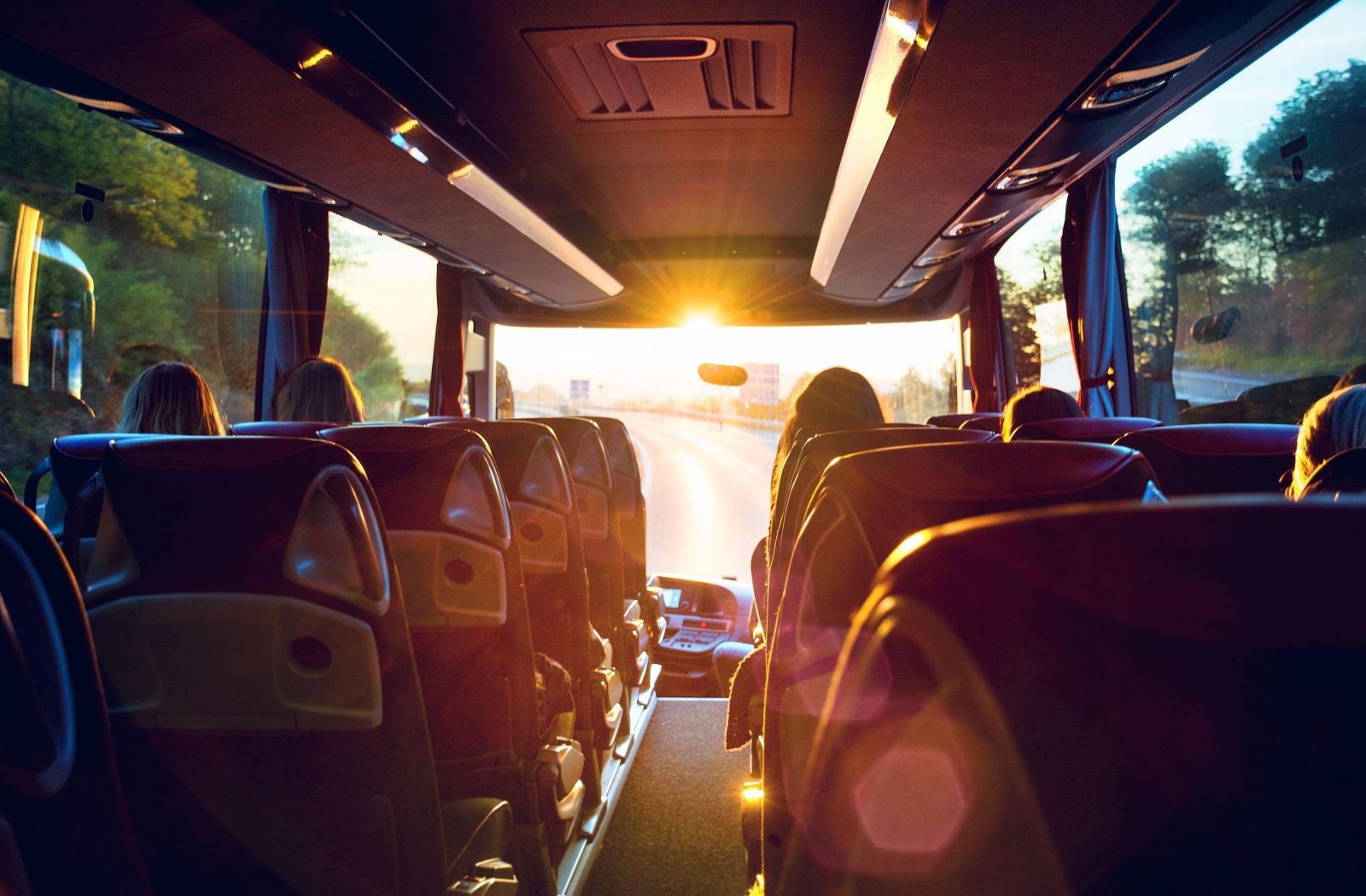 View out the front of a tour bus from inside with the sun shining warmly on the seats.