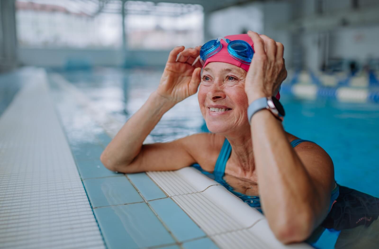 An older adult smiling while leaning against the edge of a pool preparing for their water aerobics clas