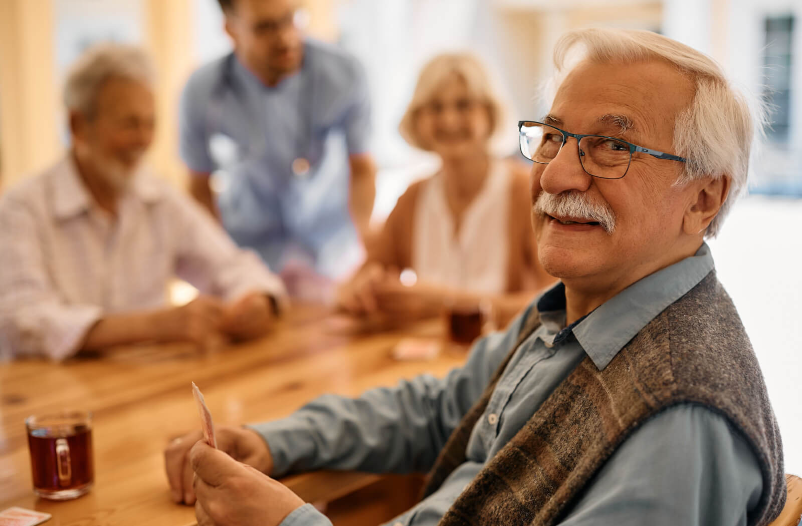 A close-up of a smiling older adult playing cards with other residents in a senior living community.