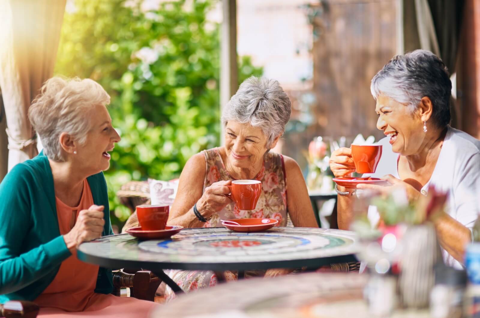 A happy group of older adults in a coffee shop socializing over a cup of tea.