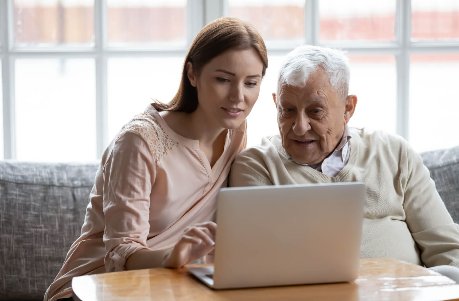 An older adult and his adult child sitting together in front of a laptop, researching assisted living communities nearby.